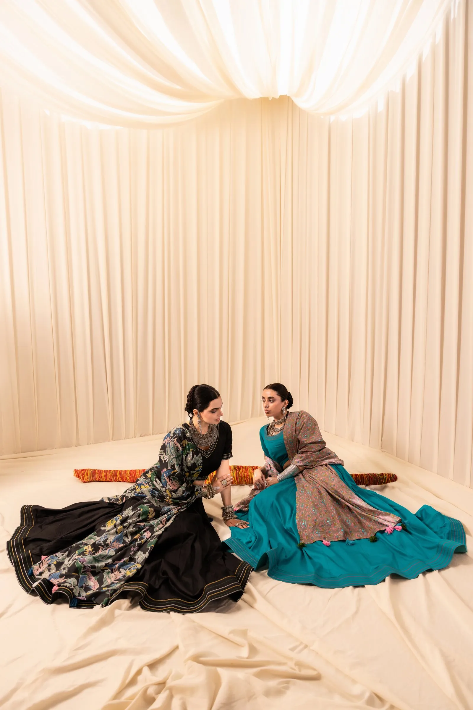 Ivory fabric draped overhead and over the walls and floor, with two models seated in lehengas